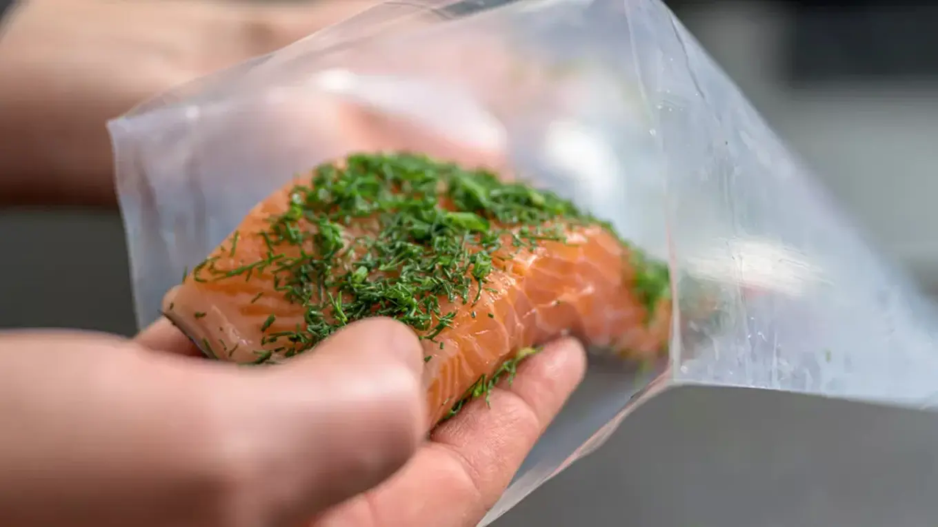 hand füllt fischfilet mit kräutern in einen vakuumbeutel