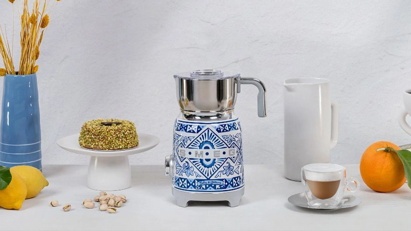 smeg dolce & gabbana blue mediterraneo milchaufschäumer smeg dolce & gabbana blue mediterraneo milchaufschäumer in blau-weiß mediterran stil neben einem milchkaffee und kuchen
