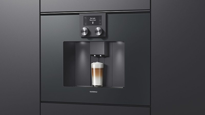 schwarzer gaggenau serie 200 kaffeevollautomat  mit einem vollen latte macchiato glas von der seite in einer schwarzen front