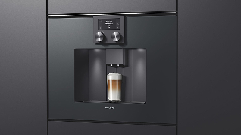Gaggenau Serie 200 Kaffeevollautomat schwarzer gaggenau serie 200 kaffeevollautomat mit einem vollen latte macchiato glas von der seite in einer schwarzen front