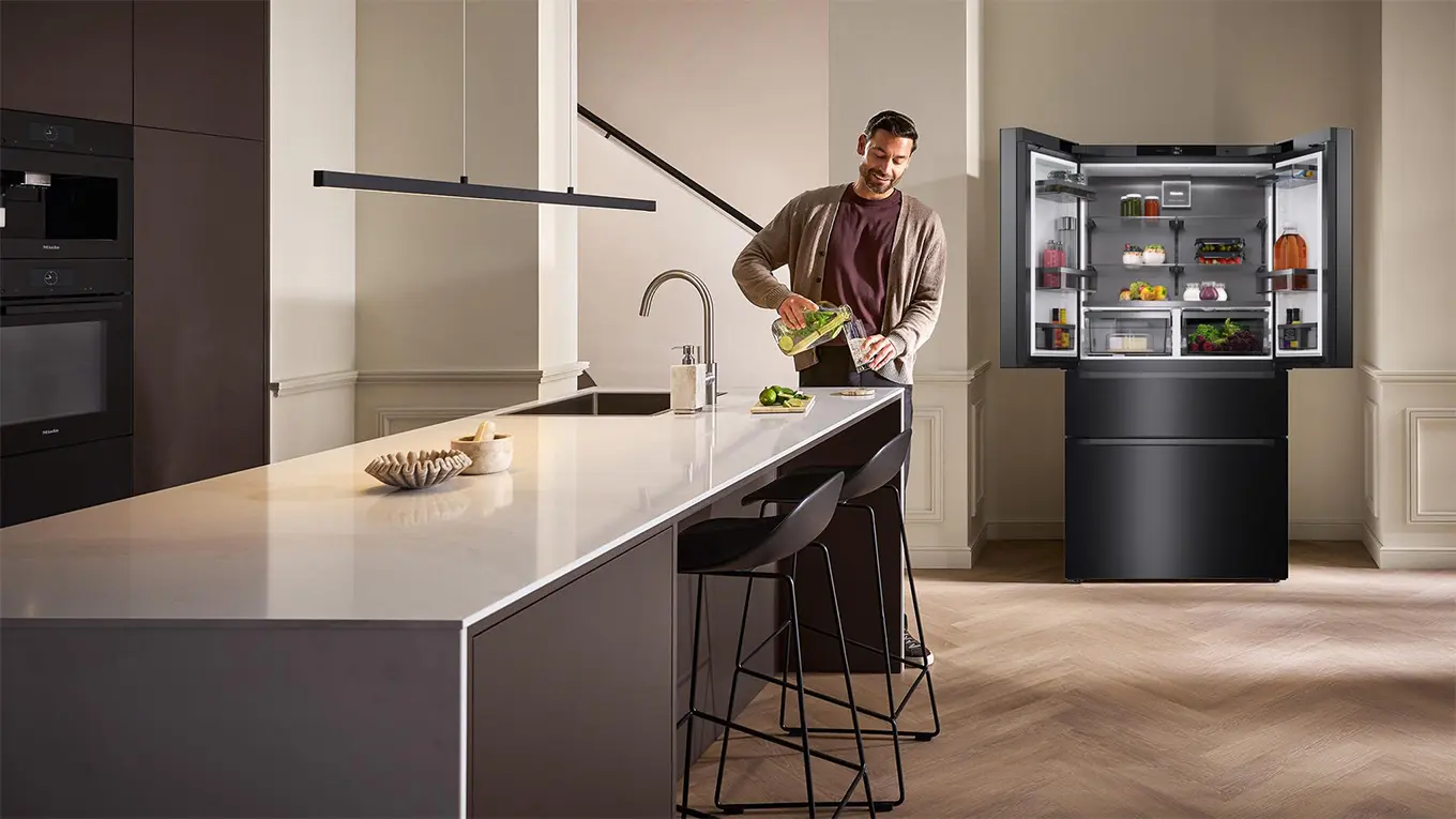 Mann steht in einer küche mit kochinsel und miele kffd 6867 kühl-gefrierkombination im hintergrund