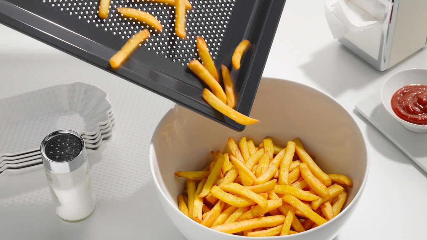 pommes aus dem airfryer pommes werden vom airfryer backblech in eine schüssel geschüttet