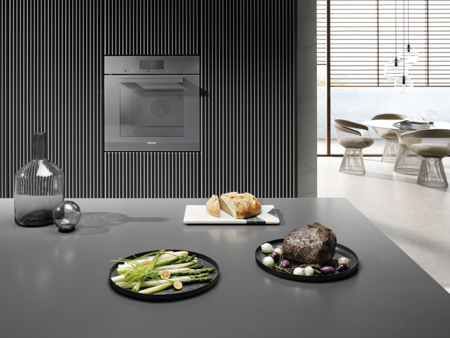 Miele 3-in-1 Prinzip Lebensmittel auf zwei schwarzen Tellern vor einem Miele Backofen mit 3-in-1 prinzip
