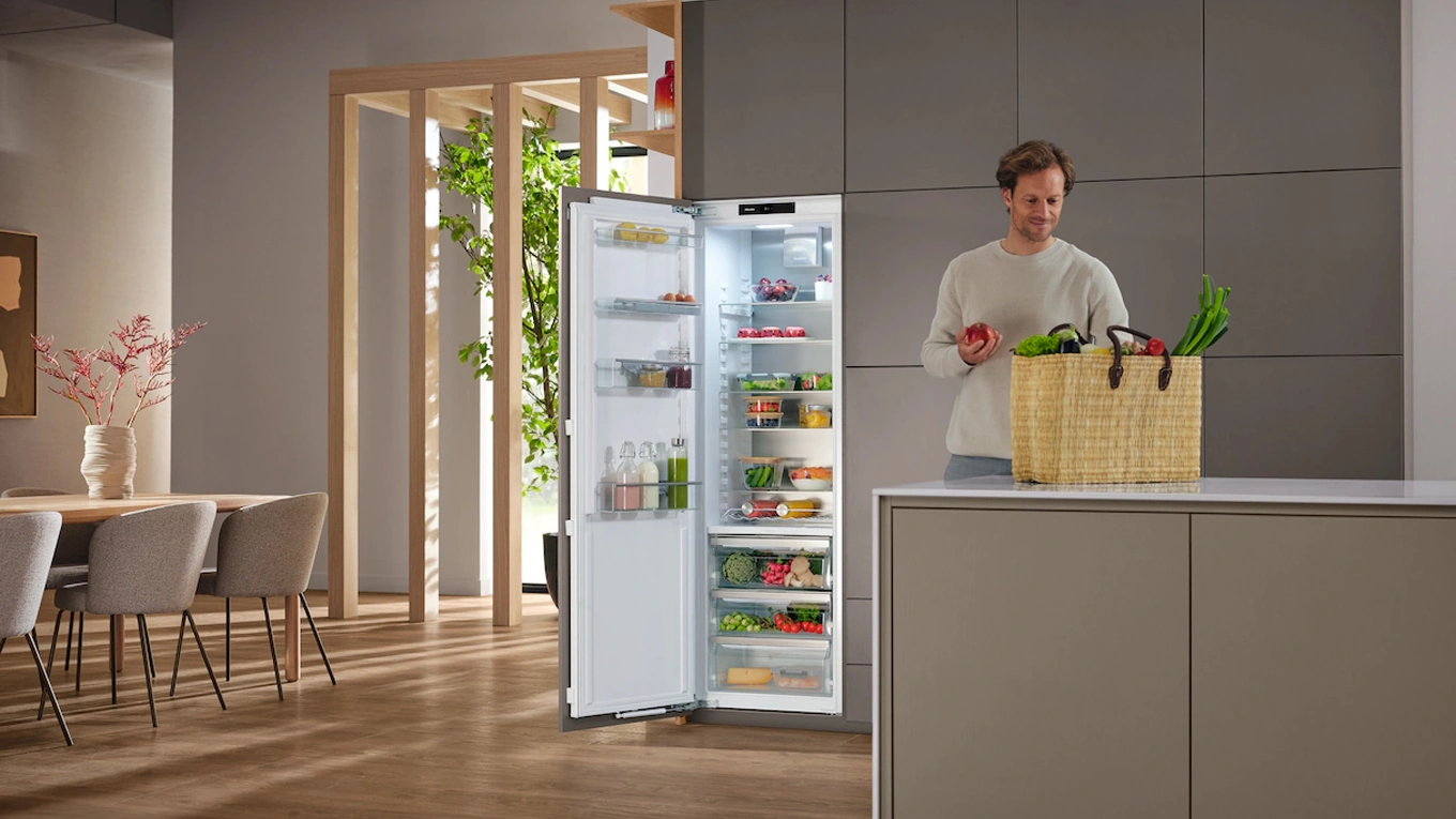 Miele K 7747 C 125 Gala Edition Kühlschrank Mann steht an einer kücheninsel mit einkäufen vor einem geöffneten Miele K 7747 C 125 Gala Edition Kühlschrank