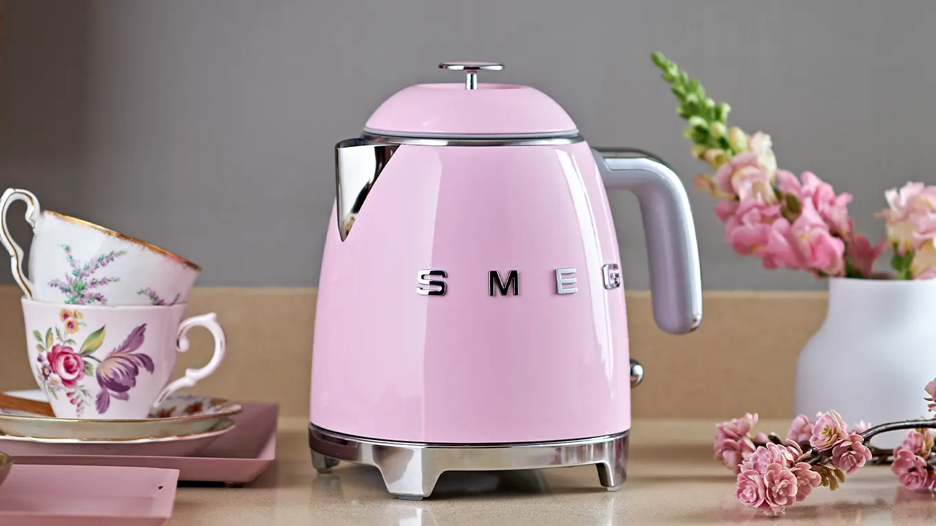smeg mini wasserkocher in cadillac pink neben gleichfarbigen blumen und geschirr mit blumenmuster
