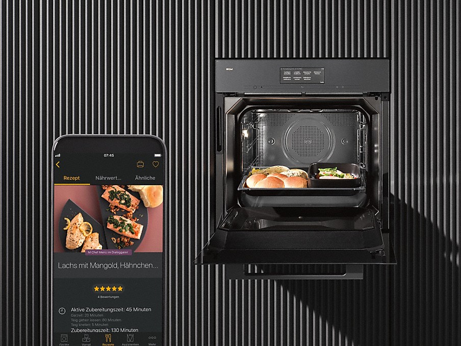 Smartphone mit Miele app auf dem Display neben einem Einbau Backofen mit geöffneter Tür