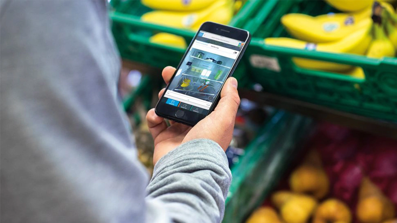 Siemens Home Connect Kühlschrank Steuerung Smartphone mit siemens home connect kühlschrank auf dem Display vor einem Obstregal im Supermarkt