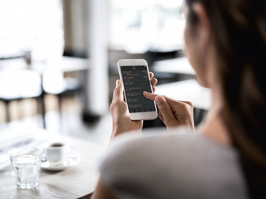Miele at home App frau von hinten beim bedienen des smartphone mit der miele app auf dem display