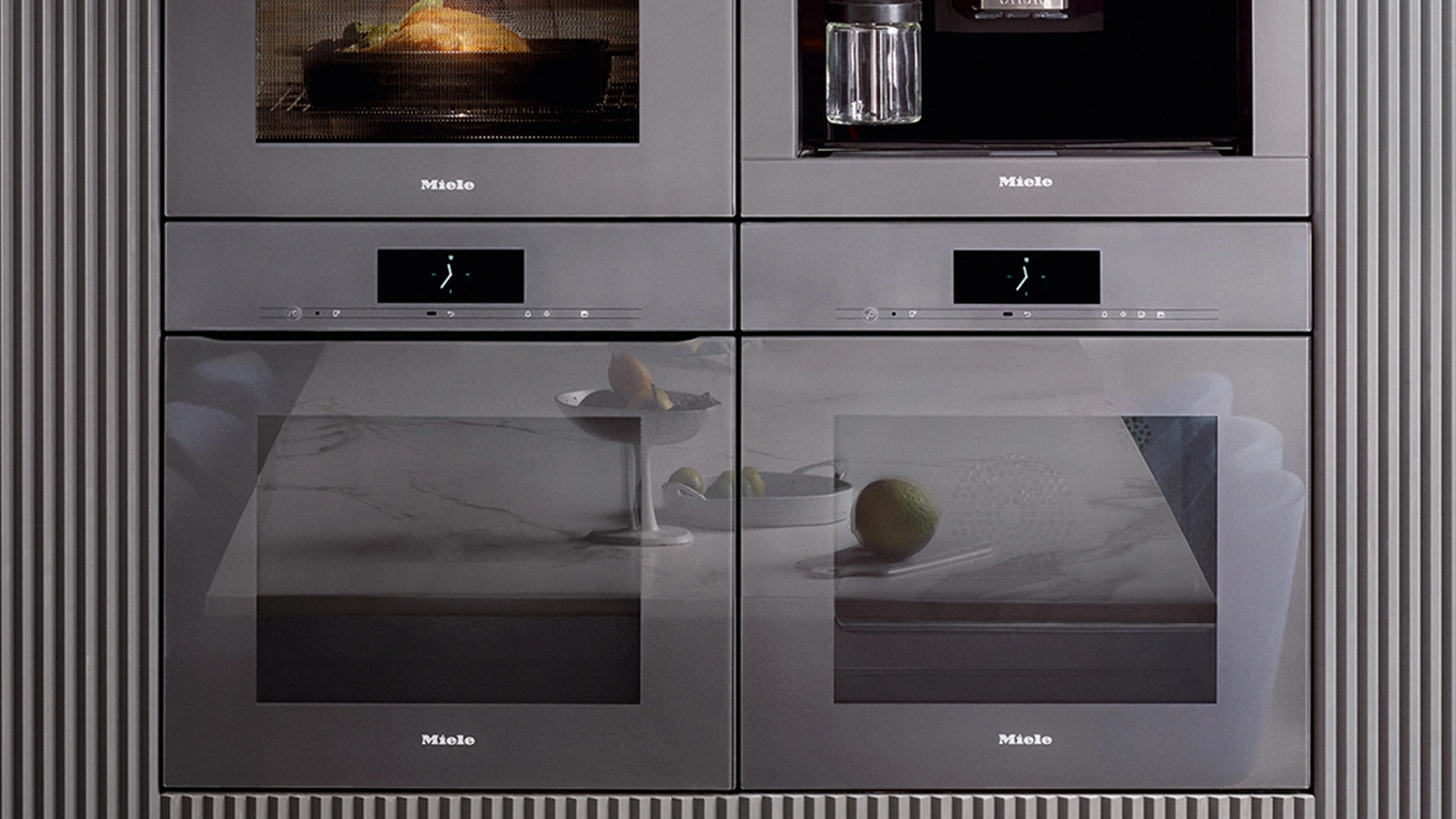 Vier Miele generation 7000 einbaugeräte aus der serie artline in silber übereinander in einer grauen küchenfront
