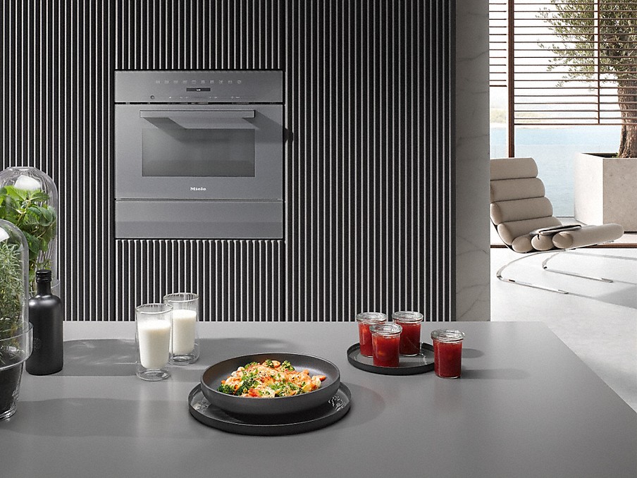 Miele Kombi-Betrieb arrangierte lebensmittel auf einer grauen arbeitsplatte vor einem einbau-kombi-backofen von miele