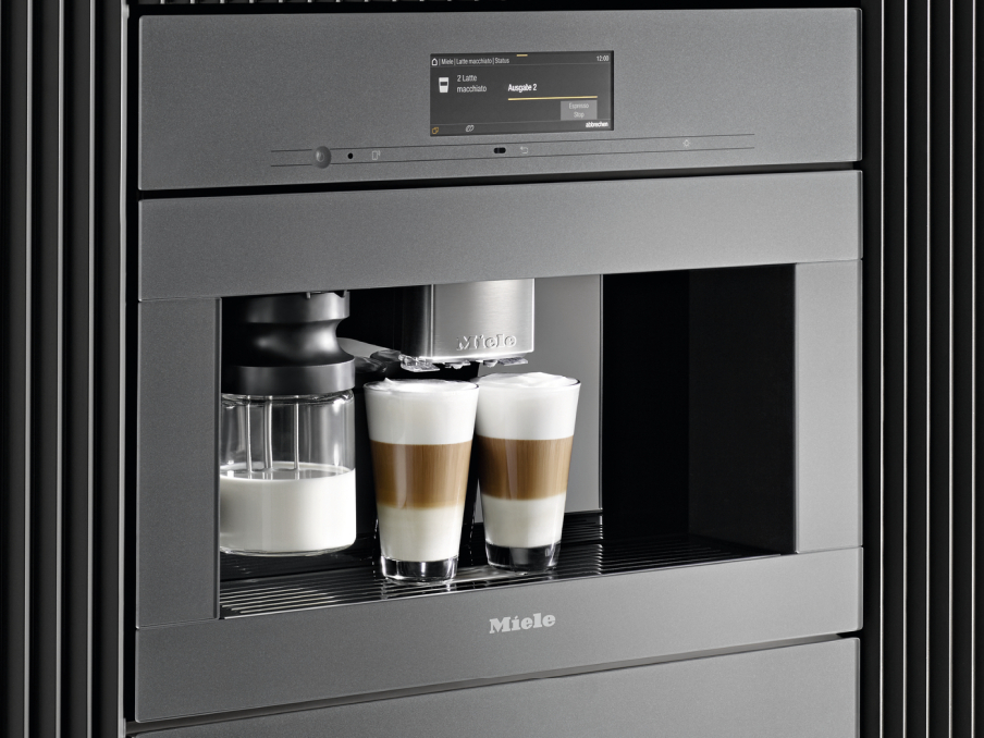 zwei gefuellte latte macchiato glaeser neben milchsystem unter einem miele kaffeevollautomat mit one touch for two funktion