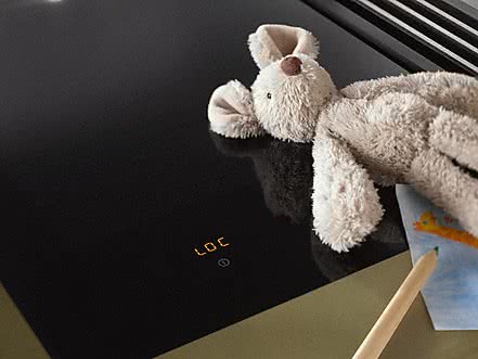 Miele Kindersicherung mit Schriftzug LOC in der Bedienleiste neben einem Teddy Kuscheltier