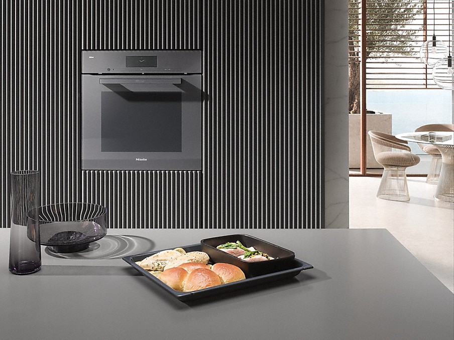 Miele M Chef Menü angerichtete speisen auf dunklem geschirr auf einer arbeitsplatte vor einem miele backofen mit m chef menü einstellung