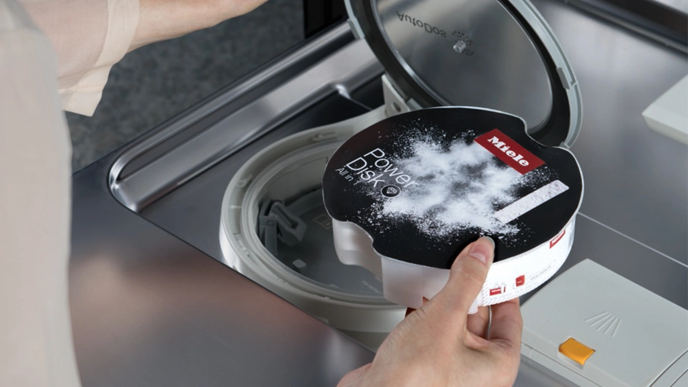 miele geschirrspüler mit autodos und power disk Powerdisk in der Hand über der Einsteckplatte beim Miele AutoDos Geschirrspüler