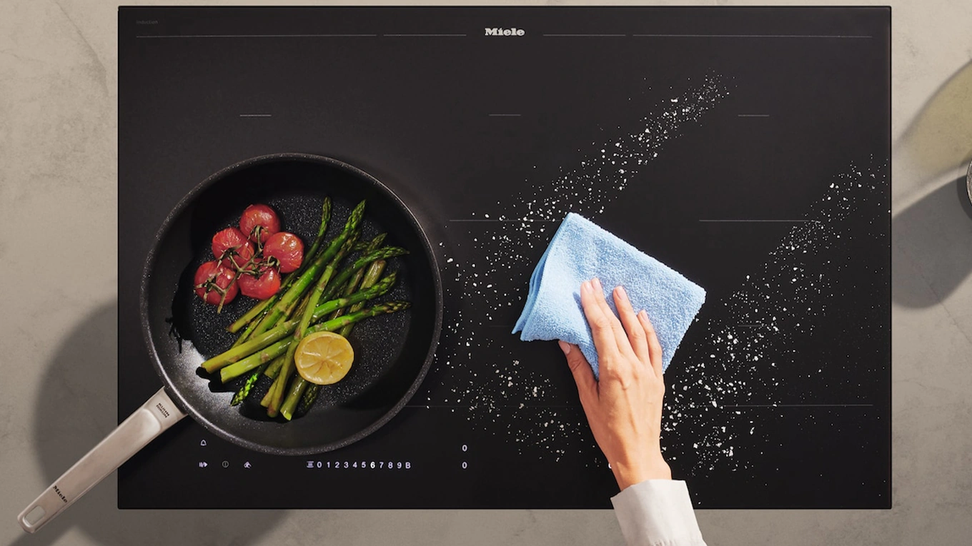 Miele kmda 7576 fl kochfeld mit dunstabzug in mattFinish Salzkrümel werden mit einem blauen mikrofasertuch vom miele mattfinish kochfeld weggewischt