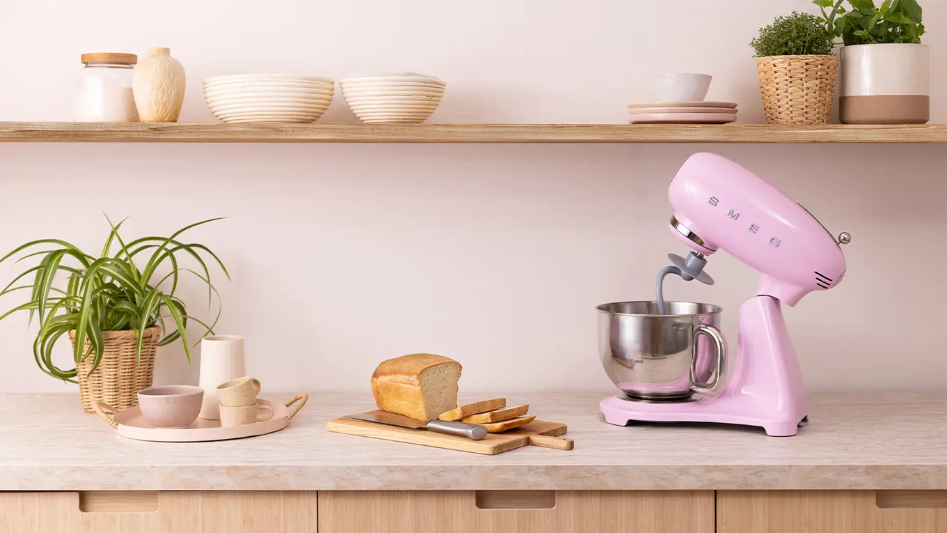 smeg küchenmaschine smf05 in cadillac punk auf einer arbeitsplatte neben geschnittenem brot auf einem holzbrett