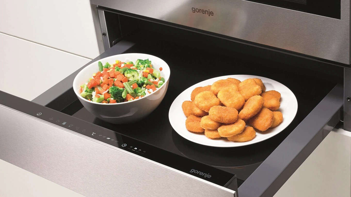 Gorenje Wärmeschublade zum Warmhalten von Speisen Teller mit Nuggets und Schüssel mit Gemüse in einer silbernen Wärmeschublade zum Warmhalten von Gorenje
