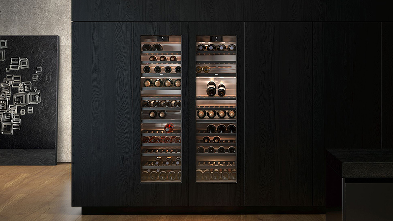 Gaggenau Serie 400 Vario Weinkühlschrank Zwei volle Vario Weinschraenke aus der Gaggenau Serie 400 mit leuchtendem warmen Licht in einer dunklen kueche
