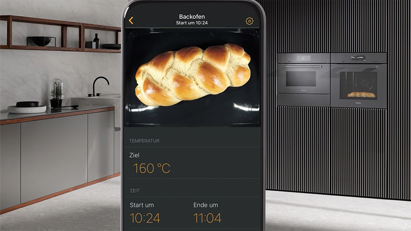 miele backofen g7000 mit kamera food view smartphone mit einem hefezopf aus der miele app auf dem display mit miele g7000 backöfen mit foodview im hintergrund