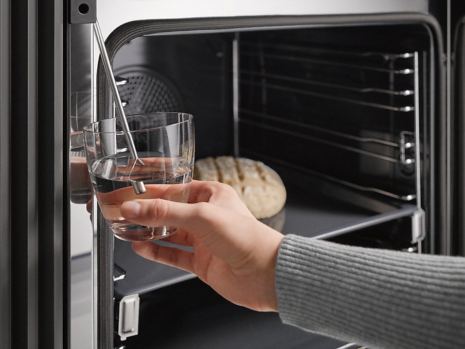 glas mit wasser vor einem miele backofen mit klimagaren für brot zum beispiel