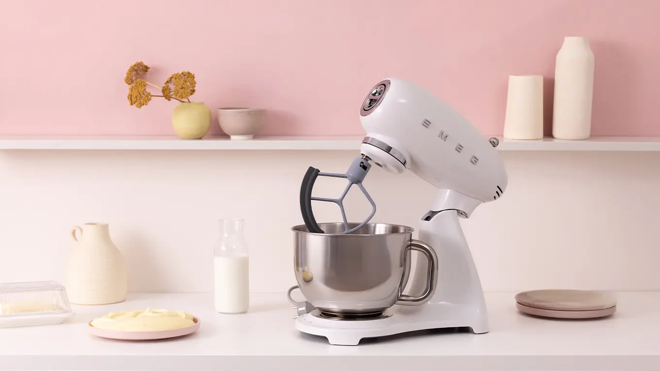weiße smeg küchenmaschine smf05 auf einer hellen arbeitsplatte neben keramik geschirr