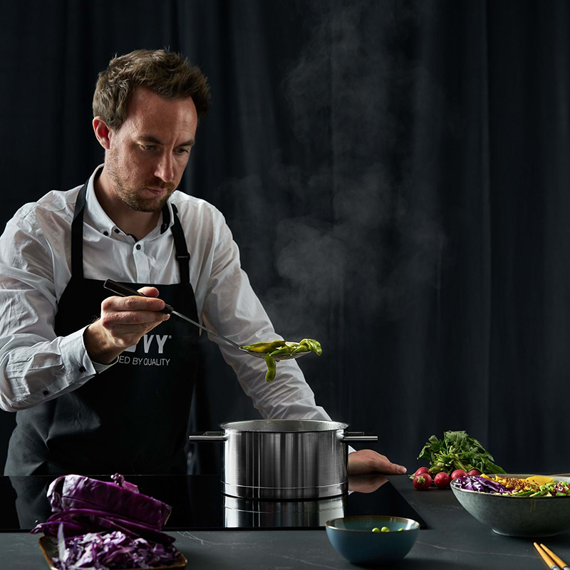 koch mit schwarzer novy schuerze beim kochen mit einem edelstahl topf