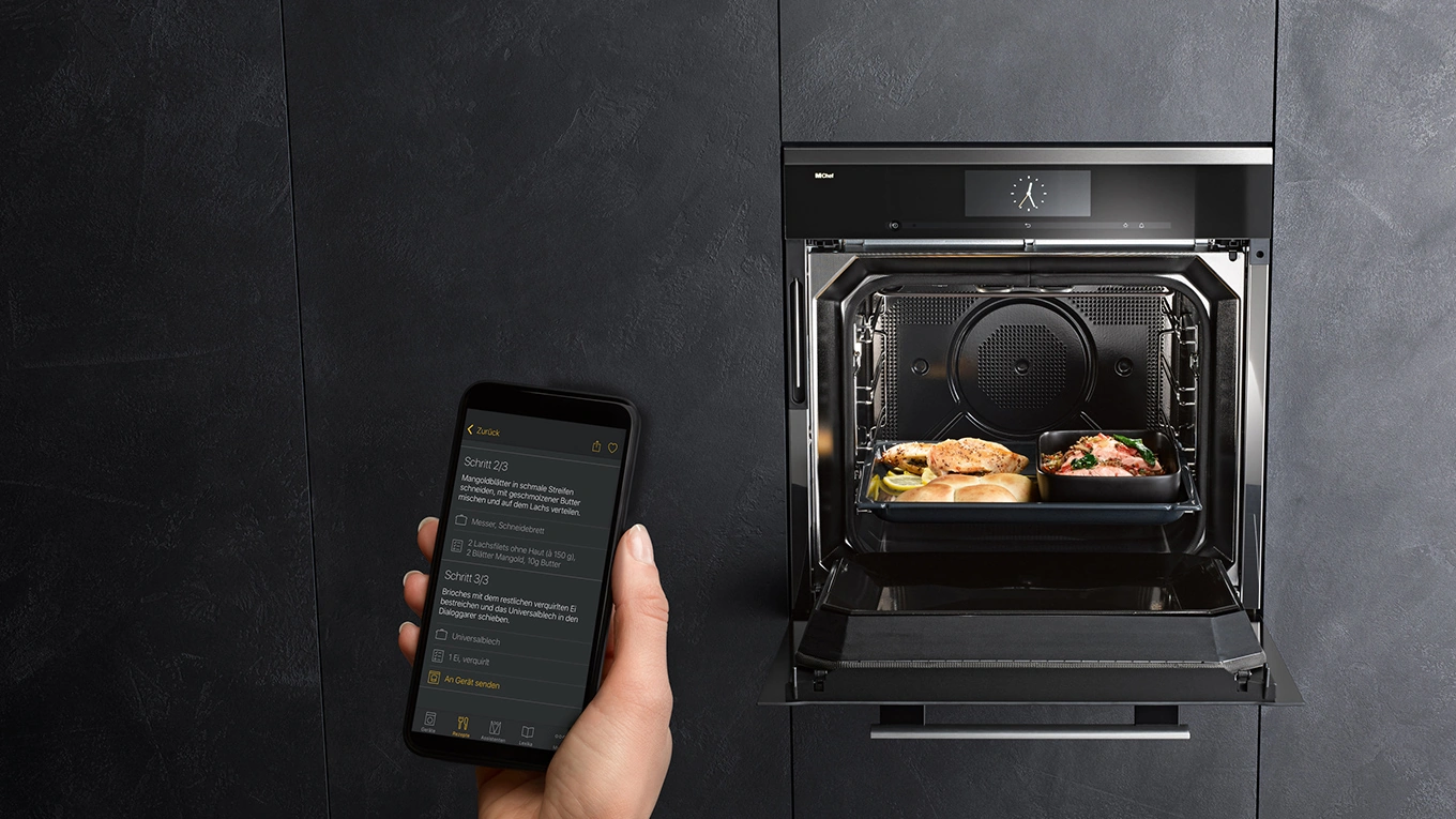 Miele Home Connect Beispiel mit Smartphone vor einem geöffneten Miele Backofen in einer schwarzen Küchenfront