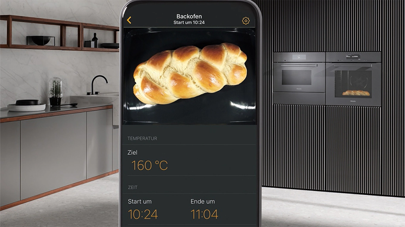 smartphone mit einem hefezopf aus der miele app auf dem display mit miele g7000 backöfen mit foodview im hintergrund