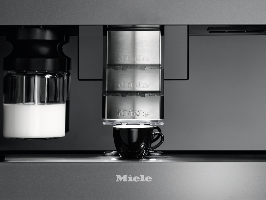 miele einbau-kaffeevollautomat mit verstellbarem cupsensor und einer schwarzen tasse neben einer milchkanne