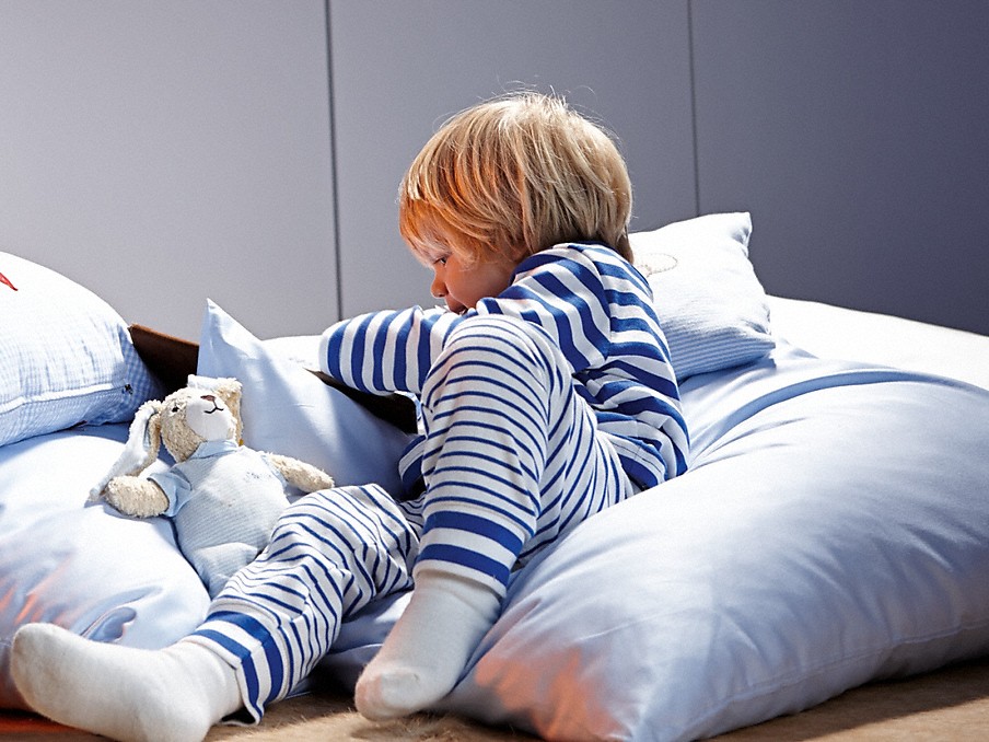 kleinkind im blau-weiß gestreiftem schlafanzug mit kuscheltier auf kissen