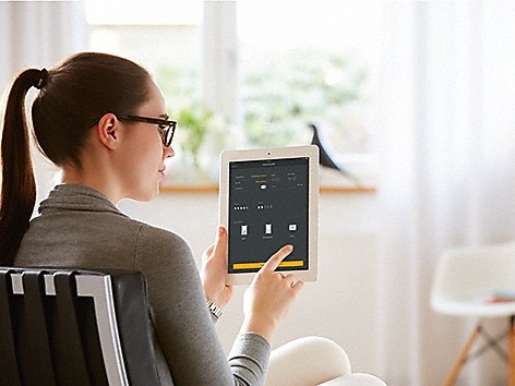 Miele At Home Frau mit Pferdeschwanz und Brille, die ein Tablet mit Miele At Home App auf dem Display hält